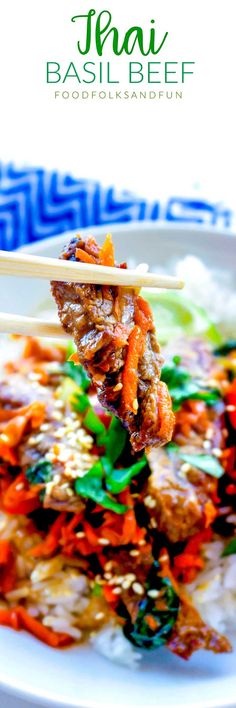 a white plate topped with meat and veggies on top of rice next to chopsticks