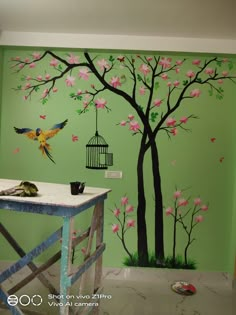 a green wall with pink flowers painted on it and a birdcage hanging from the tree