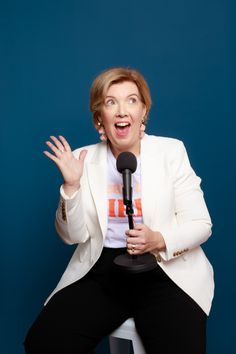 a woman sitting on top of a stool holding a microphone in her hand and making a funny face