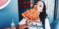 a woman eating a large slice of pizza in front of a soda bottle and wall