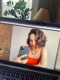 a woman looking at her cell phone while sitting in front of a laptop computer screen