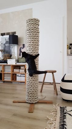 a black cat climbing on top of a scratching post in a living room next to a table