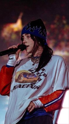 a man with long hair wearing a hat and holding a microphone in his hand while standing on stage