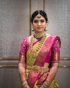 a woman wearing a green and pink sari with gold jewelry on her neck, standing in