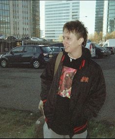 a man standing in the middle of a parking lot next to tall buildings and parked cars