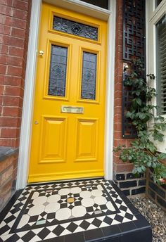 a yellow front door with black and white tiles on the ground next to a brick building