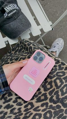 a person holding a pink cell phone case on top of a leopard print chair next to a white bench