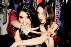 two young women making the v sign with their hands while standing in front of a rack of clothes