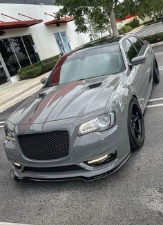 the front end of a grey car parked in a parking lot next to a building