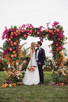 a bride and groom kissing under a floral arch