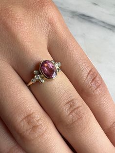 A vibrant Pink tourmaline is set in Emily's 14k gold Trefoil cluster setting with a freeform band. We originally saw this as being a unique engagement ring but it would be just as wonderful as an everyday bit of sparkle and looks phenomenal with our halo bands Approximate stone size: 9mm x 7mm TCW tourmaline: 1.2ct TCW diamonds: .12ct Mohs Stone Hardness: 7.5-8 This piece is handmade to order in Emily's Hudson Valley studio. Please allow for slight variations in stone color, size and shape. Plea Heirloom Pink Sapphire Ring, Elegant Yellow Gold Tourmaline Birthstone Ring, Heirloom Oval Pink Sapphire Rings, Heirloom Pink Sapphire Oval Rings, Elegant Ruby Birthstone Ring With Tourmaline, Gold Tourmaline Ring With Rose Cut Diamonds, Yellow Gold Tourmaline Rings With Rose Cut Diamonds, Yellow Gold Tourmaline Jewelry With Rose Cut Diamonds, Tourmaline Jewelry In Yellow Gold With Rose Cut Diamonds