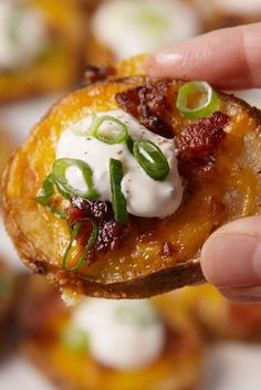 a hand holding up a potato that is topped with sour cream and green onion slices