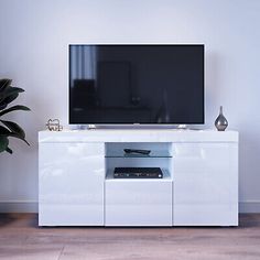 a white entertainment center with a flat screen tv on it's stand and a potted plant next to it