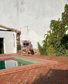 a man sitting in a chair next to a swimming pool on top of a red brick patio