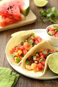 three tacos on a plate with watermelon and lime