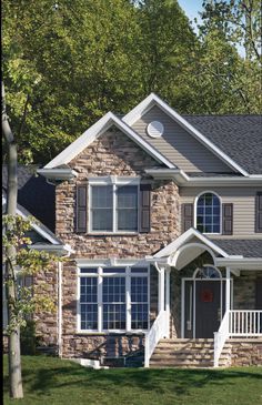 a large brick house with two story windows and white trim on the front porch, surrounded by trees