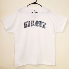 Make a statement with this simple but bold Locally Handmade white New Hampshire T-shirt. This unisex shirt is perfect those looking for souvenir wardrobe or just representing the 603. These make a great casual and comfortable look for any sporting event, tailgating, bbq or night out having a few beers with friends.   The Hanes Essentials Comfort Soft T-Shirt is a 100% 5.2oz cotton t shirt. It's made for comfort and style, with breathable material and a cut that always lays well. That's because of the double-needle stitching, shoulder-to-shoulder tape, and the cover-seamed neck, all of which work together to make sure your shirt always looks good. Everything about this shirt, including sleeve length, neck design, and collar, is all designed to ensure this shirt feels as good as it looks. We White Slogan T-shirt For College, White Cotton Shirt With Lettering, White Fan Apparel T-shirt With Lettering, White Graphic Tee Shirt With Lettering, White College T-shirt With Lettering, White Casual T-shirt With Lettering, White Cotton T-shirt With Lettering, White T-shirt With Lettering For Streetwear, White Lettering T-shirt For Streetwear