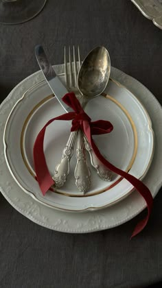 a plate with silverware and red ribbon tied around the edge, on top of a black table cloth