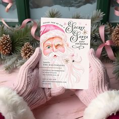 a pink santa clause holding up a book in front of some christmas decorations and pine cones