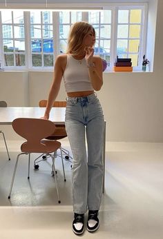 a woman standing in front of a table talking on a cell phone while wearing high waist jeans