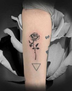 a black and white photo of a rose with an arrow tattoo on the left arm