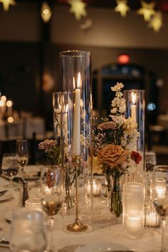 a table with candles and flowers in vases next to wine glasses on the table