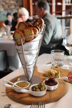 bread and olives in small bowls on a wooden platter at a restaurant table