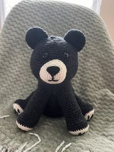 a crocheted black bear sitting on top of a chair next to a window