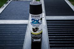 a can of black paint sitting on top of a metal grate with grass in the background