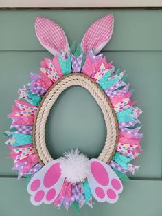 a pink and green wreath with bunny ears hanging on the front door, decorated with paper