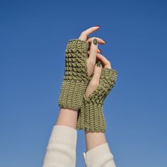 two hands in knitted mittens reaching up into the sky with their fingers together