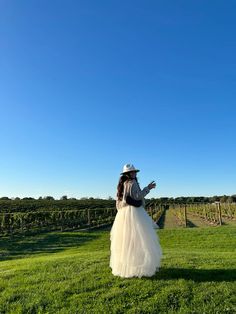 a woman in a long white dress and hat is standing on the grass with her arms outstretched