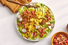 a large salad on a white plate next to two small bowls filled with fruit and veggies