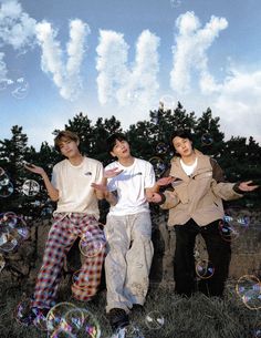 three young men are standing in the grass with soap bubbles floating over them and trees behind them