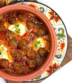 a bowl filled with meatballs and sauce on top of a wooden cutting board next to bread