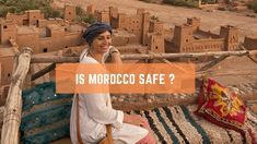 a woman sitting on top of a bed in front of a desert town with the words is morocco safe?