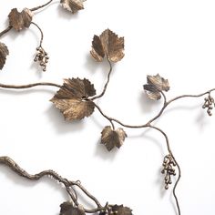 a metal sculpture with leaves and berries hanging from it's sides on a white wall