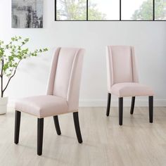 two pink chairs sitting next to each other in front of a white wall with windows