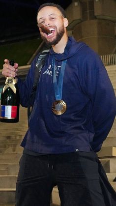 a man with a beard holding a bottle of wine and wearing a medal around his neck