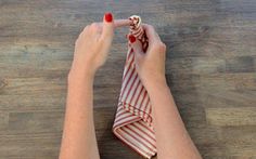 a woman's hands holding a red and white striped napkin on top of a wooden table