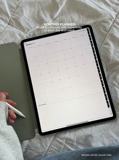 a person's hand holding a pen next to a planner on top of a bed