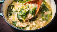 a wooden spoon in a pot filled with beans and spinach soup on top of a table