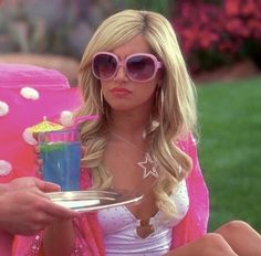 a woman in pink sunglasses holding a plate with a drink on it and another person sitting down behind her