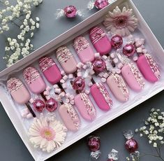 pink and white decorated nails in a box with flowers on the table next to it