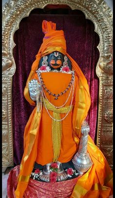 the statue is dressed in an orange outfit with beads on it's head and body