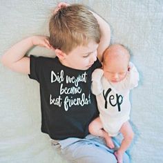 a young boy laying on top of a bed next to a baby wearing a t - shirt