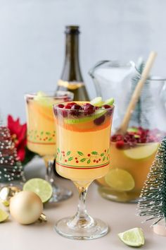 two glasses filled with fruit and garnish sitting on a table next to christmas decorations