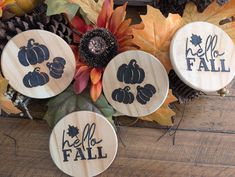 three wooden pumpkins with the words hello fall painted on them and some autumn leaves