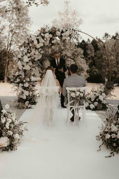 a bride and groom sitting at the end of their wedding ceremony in front of an arch decorated with white flowers