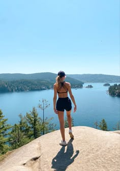 a woman standing on top of a rock next to a body of water with trees in the background